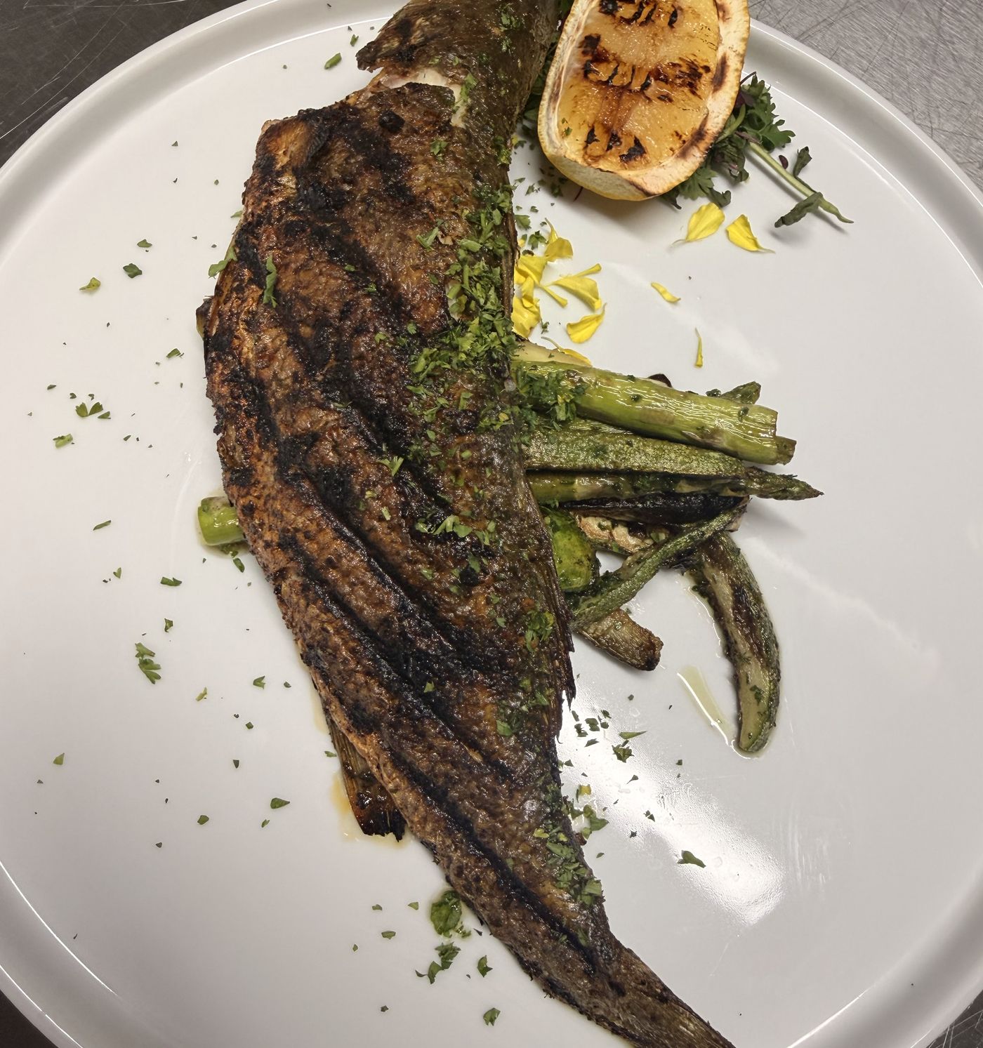 A whole grilled branzino with charred skin, grilled asparagus and a lemon half.