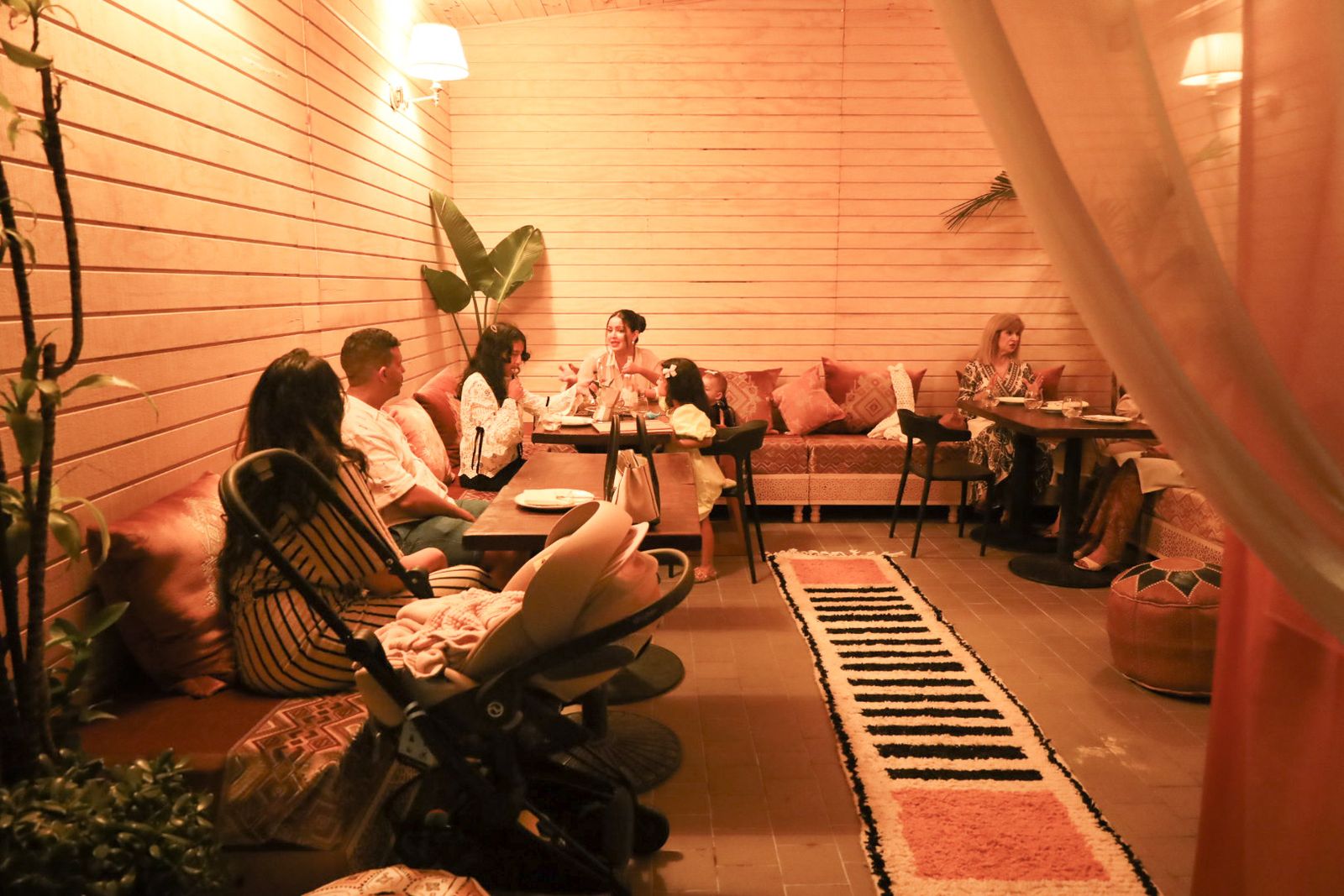 Guests at low banquettes in the warm-lit lounge, a kilim runner down the centre of the room.