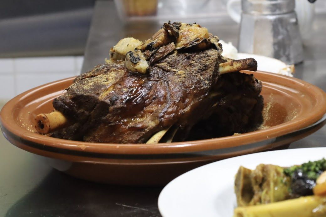 A whole braised lamb shoulder in an unglazed clay dish.