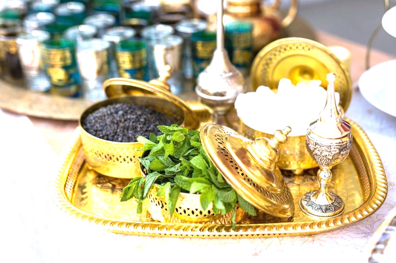 A gold mint tea service on a brass tray with fresh mint and small glasses.